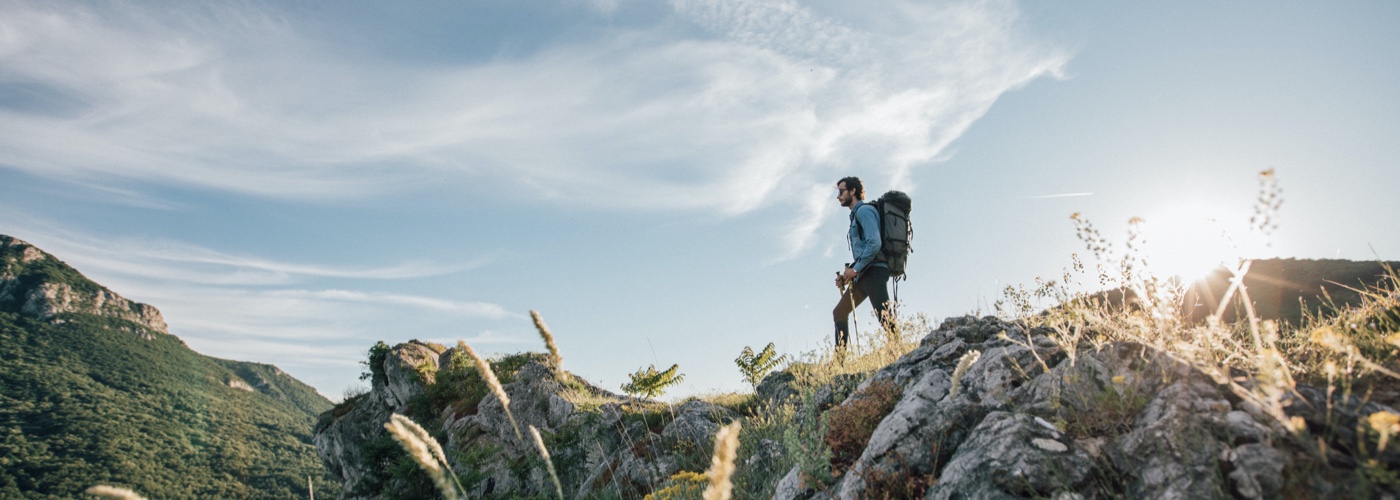 A man wearing hiking backpack standing in sunrise spring rays peaking through forest